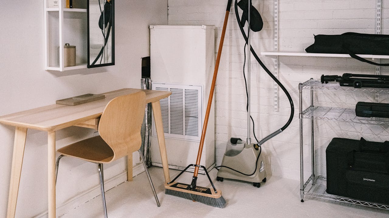 services-01 A tidy home office space featuring a wooden desk, chair, broom, and cleaning equipment.